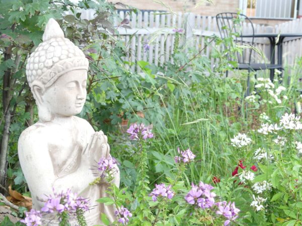 Statue eines meditierenden Buddhas mit den Händen in der Gebetshaltung in einem Garten.