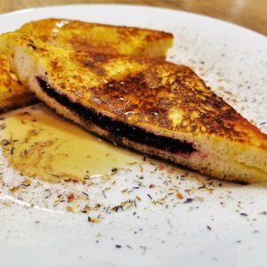 French-Toast diagonal halbiert, serviert auf einem weißen Teller, bestreut mit Gewürzblüten und Ahornsirup.
