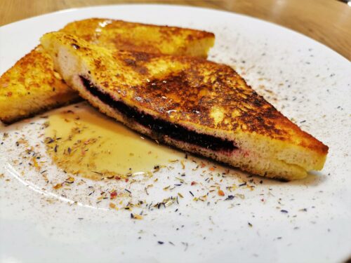 French-Toast diagonal halbiert, serviert auf einem weißen Teller, bestreut mit Gewürzblüten und Ahornsirup.