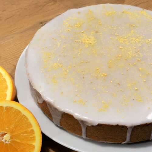 Karottenkuchen mit Zitronenglasur serviert auf weißen Teller, dekoriert mit frischen halbierten Orangen.