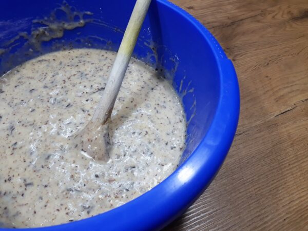 Die fertige Teigmasse für den Bananen-Nuss-Schokokuchen in einer blauen Plastikrührschüssel mit einem Holzrührlöffel.