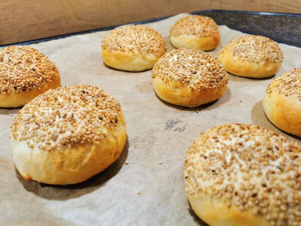 Fertig gebackene Burger Buns frisch aus dem Ofen auf einem mit Backpapier belegten Backblech.