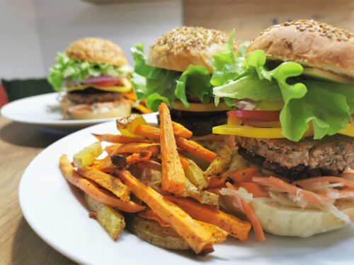 Burger gefüllt mit veganen Patties, frischem Gemüse und Coleslaw. Dazu serviert werden Pommes aus Erdäpfeln und Süßkartoffeln.