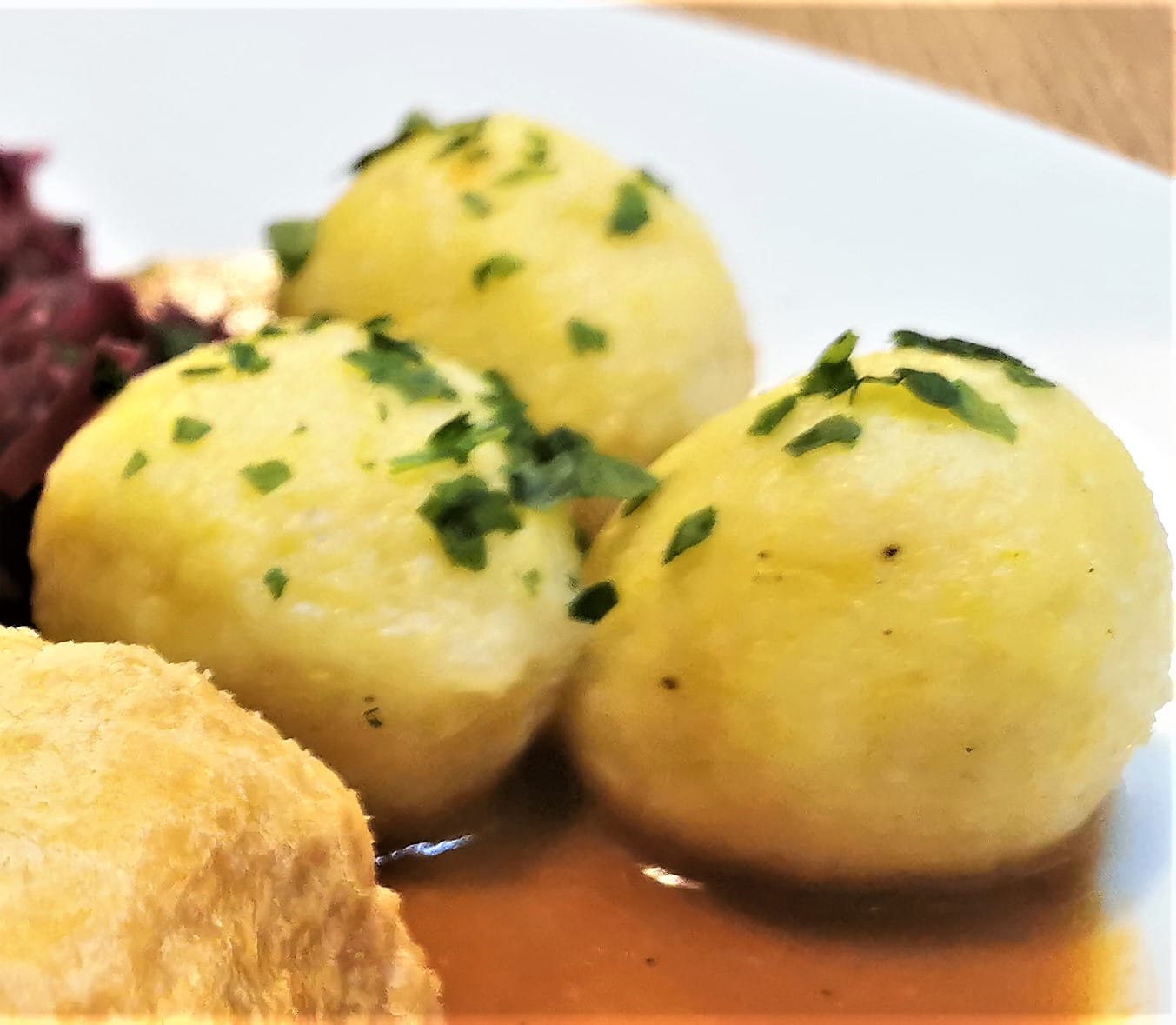 Erdäpfelknödel als Beilage zu einem Braten, mit Bratensauce und Rotkraut, serviert auf einem weißen Teller.