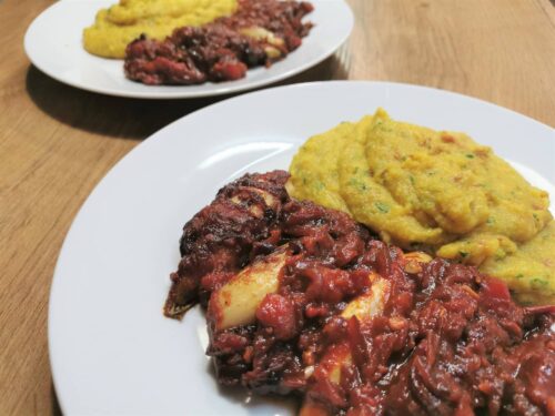 Geschmorter Chicorèe in Balsamico-Paradeisersauce mit Polenta, serviert auf einem weißen Teller.