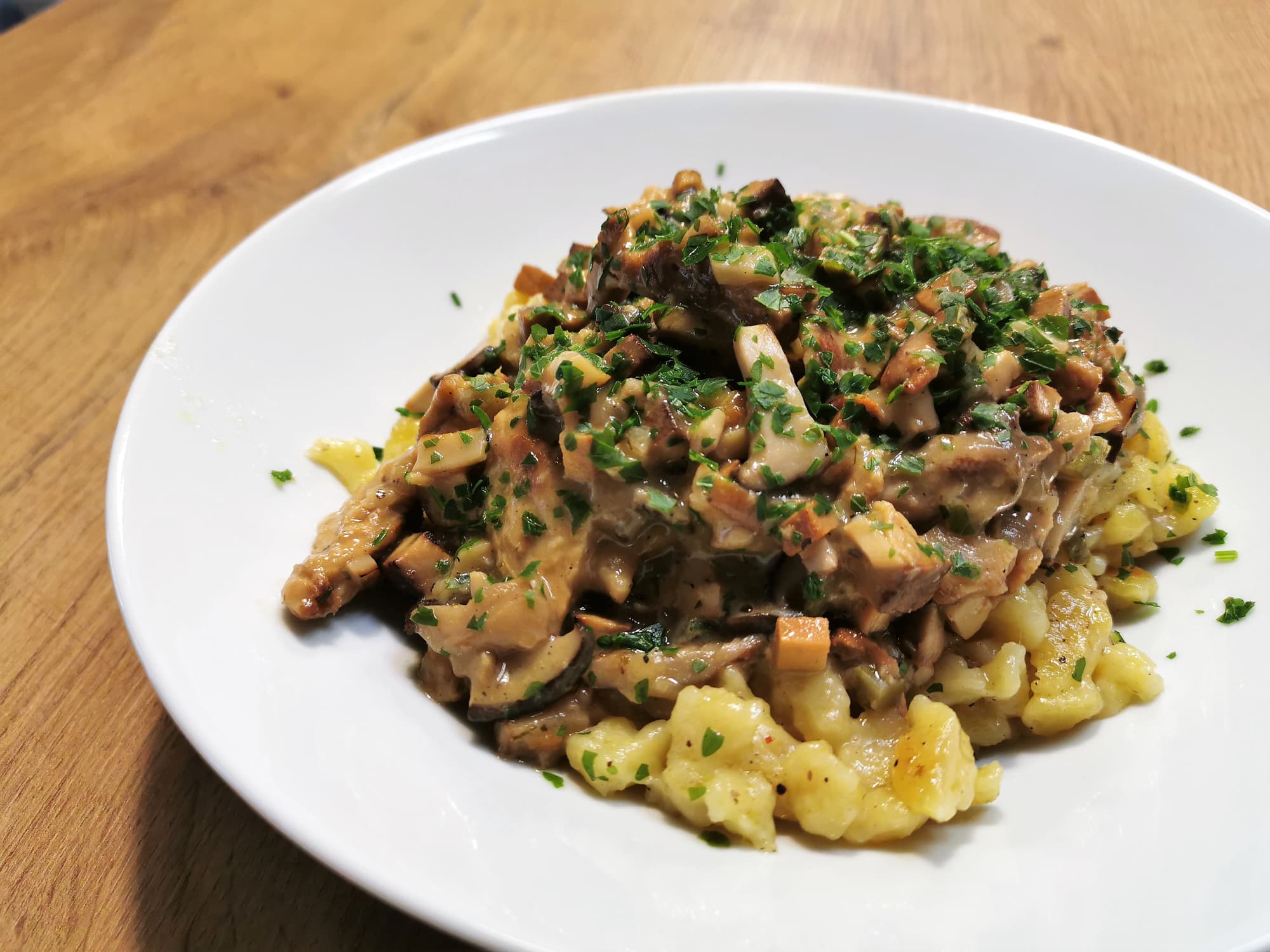 Geschnetzeltes Stroganoff Art mit Nockerl serviert auf einem weißen Teller, garniert mit frisch gehackter Petersilie.