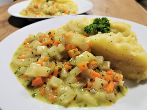 Kohlrabi Karotten Cremegemüse mit Erdäpfelpürree, serviert auf einem weißen Teller, garniert mit einer Petersilie.