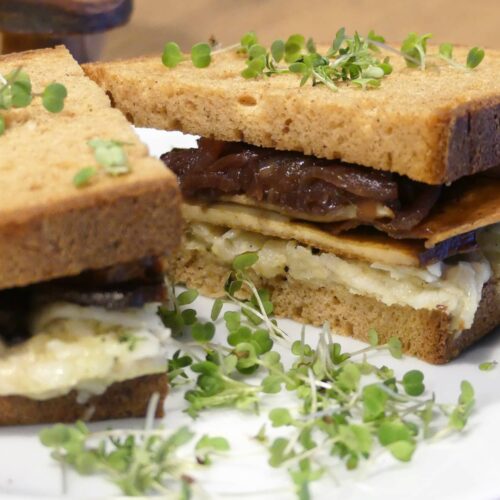 Ein aufgeschnittenes Kräuterseitling-Rettich Sandwich serviert auf einem weißen Teller und garniert mit Kresse.