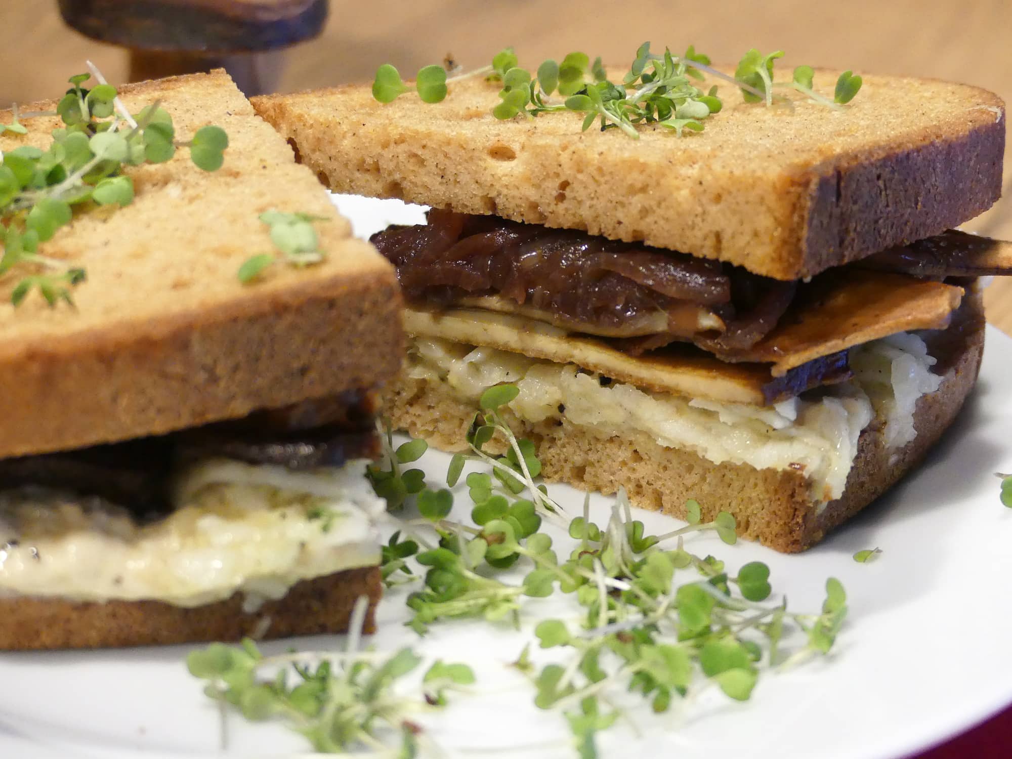Ein aufgeschnittenes Kräuterseitling-Rettich Sandwich serviert auf einem weißen Teller und garniert mit Kresse.
