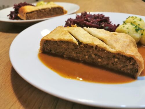 Linsenbraten auf einem weißen Teller angerichtet mit Rotkraut, Erdäpfelknöderl und Bratensauce.