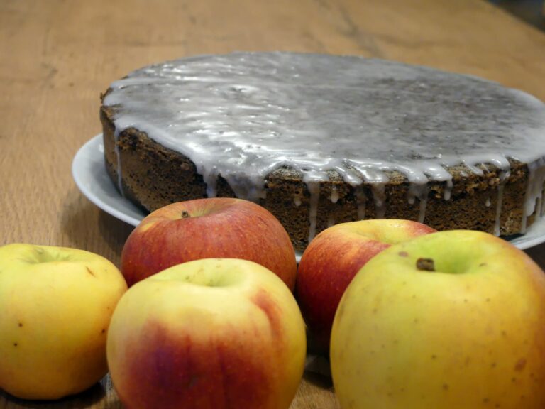 Mohn-Apfel-Kuchen mit Glasur und Äpfeln im Vordergrund