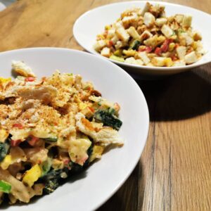 Bunter Nudelsalat angerichtet in einem weißen Teller, bestreut mit knusprigen Croutons.