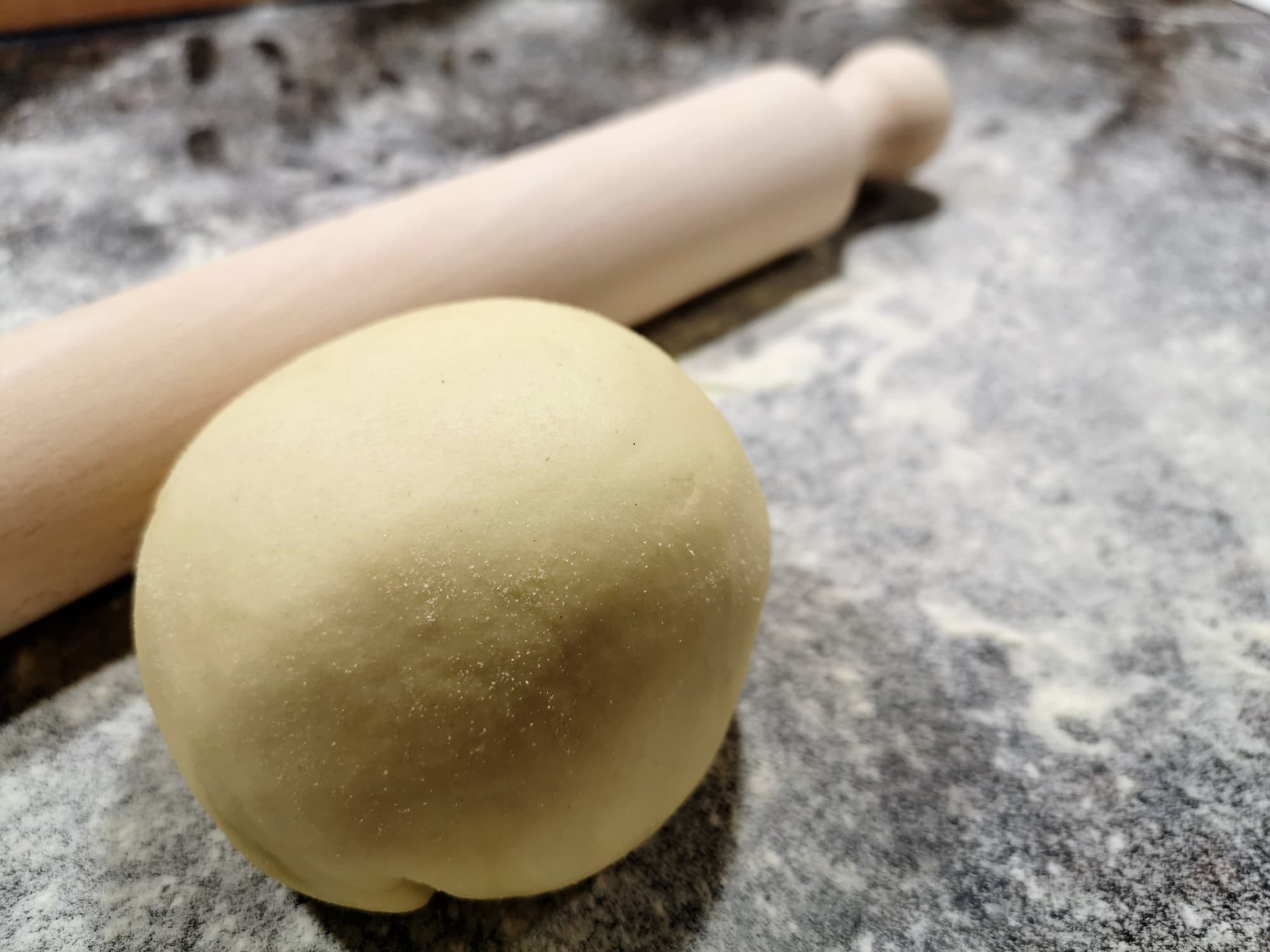 Eine Teigkugel frischer Pastateig auf einer bemehlten Arbeitsfläche mit einem Nudelholz.