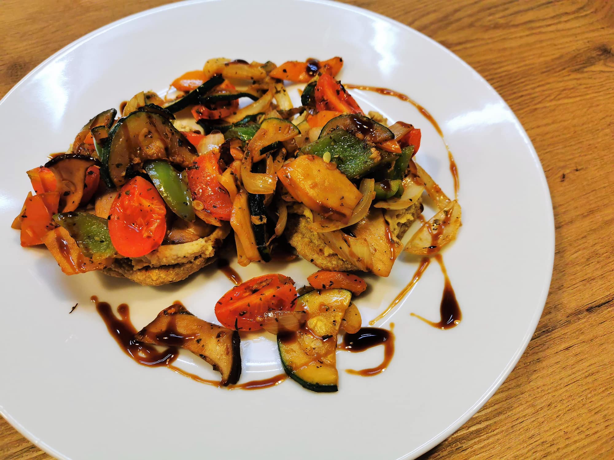 Pfannenbrot belegt mit Hummus und gebratenem mediterranem Gemüse, serviert auf einem weißen Teller und getoppt mit Crema di Balsamico.