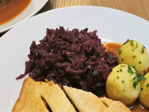 Rotkraut als Beilage serviert auf einem weißen Teller gemeinsam mit Linsenbraten, Erdäpfelknöderl und Bratensauce.