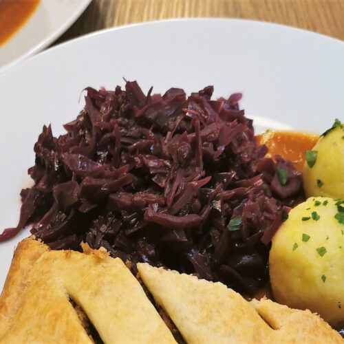 Rotkraut als Beilage serviert auf einem weißen Teller gemeinsam mit Linsenbraten, Erdäpfelknöderl und Bratensauce.