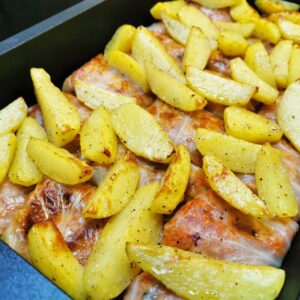 Die fertig gebratenen Sarma-Krautrouladen frisch aus dem Ofen belegt mit Erdäpfelspalten, welche mitgebraten wurden.