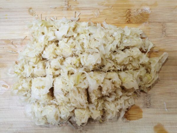 Sauerkraut auf einem Holzschneidebrett, welche kreuz und quer eingeschnitten wurde.