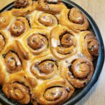 Schneckerl mit Zimt-Nuss-Rosinen Füllung und Kokos-Frosting in einer schwarzen, runden, beschichteten Backform.