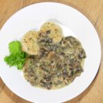 Schwammerlsauce mit Semmelknoedel serviert auf einem weißen Teller, dekoriert mit frischer Petersilie.