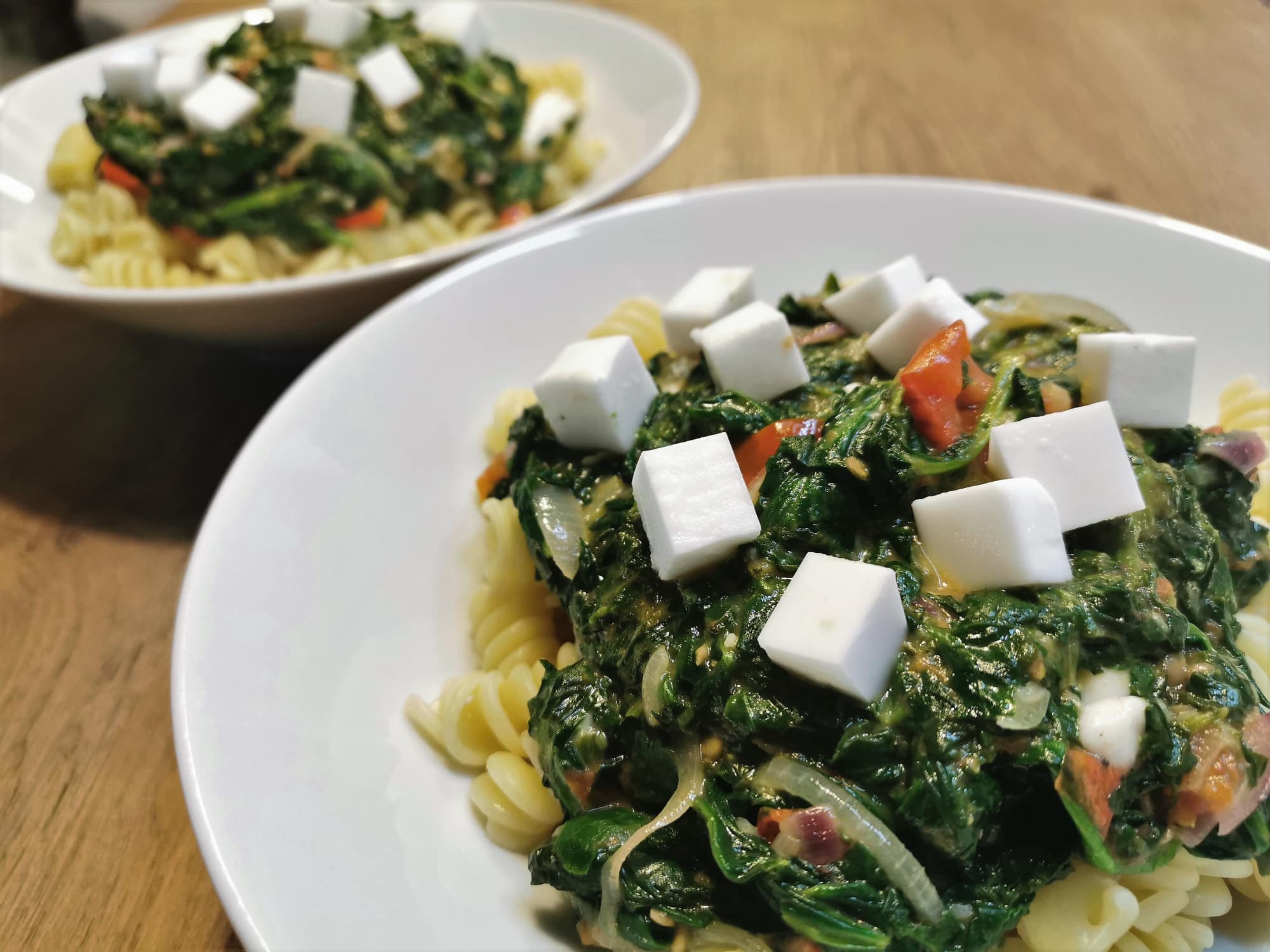 Spinat-Feta Pasta angerichtet in einem weißen Teller, getoppt mit frischen Feta-Würfeln.