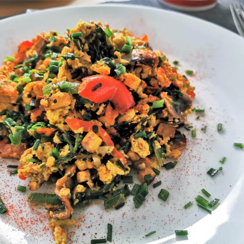 Tofu-Eierspeis mit buntem Gemüse der Saison angerichtet auf einem weißen Teller, bestreut mit frischem Schnittlauch und Chili.