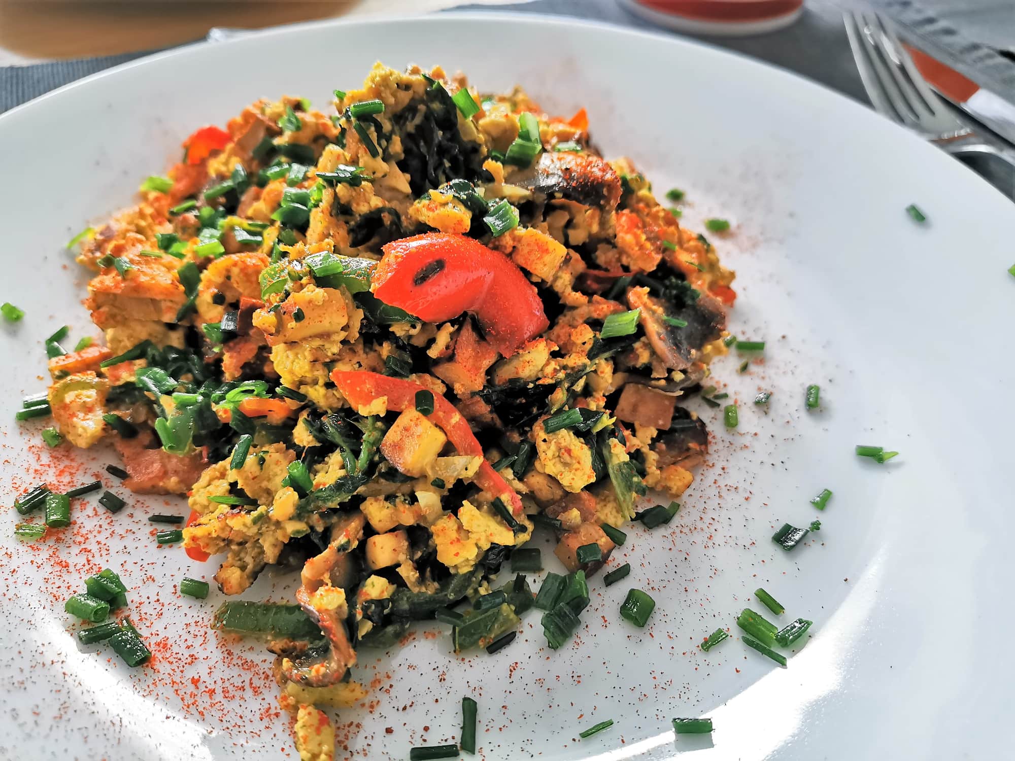 Tofu-Eierspeis mit buntem Gemüse der Saison angerichtet auf einem weißen Teller, bestreut mit frischem Schnittlauch und Chili.