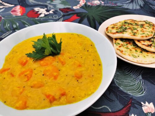 Karotten-Zwiebel-Curry mit gelben Linsen und Kokos-Knoblauch-Naan Brot angerichtet in einem grau-blauen Teller, das Naan Brot wird separat serviert.