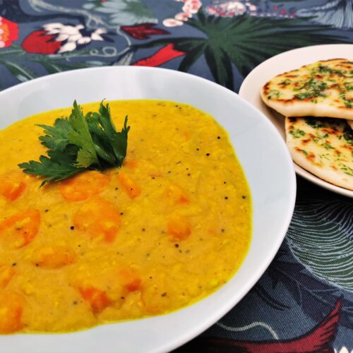 Karotten-Zwiebel-Curry mit gelben Linsen und Kokos-Knoblauch-Naan Brot angerichtet in einem grau-blauen Teller, das Naan Brot wird separat serviert.