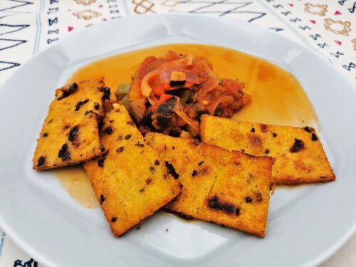 Polentaschnitten mediterran mit Gemüseragout nach Ratatouille Art angerichtet auf einem hellgrauen Teller