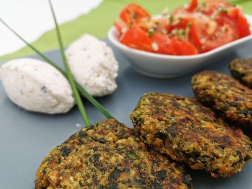 Spinat-Kichererbsen-Fritters mit Hirtenkäsedip und Paradeisersalat angerichtet auf einem graublauen eckigen Teller.