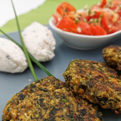 Spinat-Kichererbsen-Fritters mit Hirtenkäsedip und Paradeisersalat angerichtet auf einem graublauen eckigen Teller.