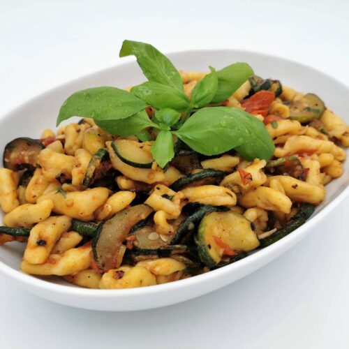 Cavatelli mit gebratenen Zucchini und Tomaten, angerichtet in einer weißen, ovalen Schale, garniert mit Basilikum.