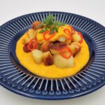 Gnocchi in Paprika-Chili-Sauce, serviert auf einem blauen Teller, garniert mit Chiliringen und Petersilie.