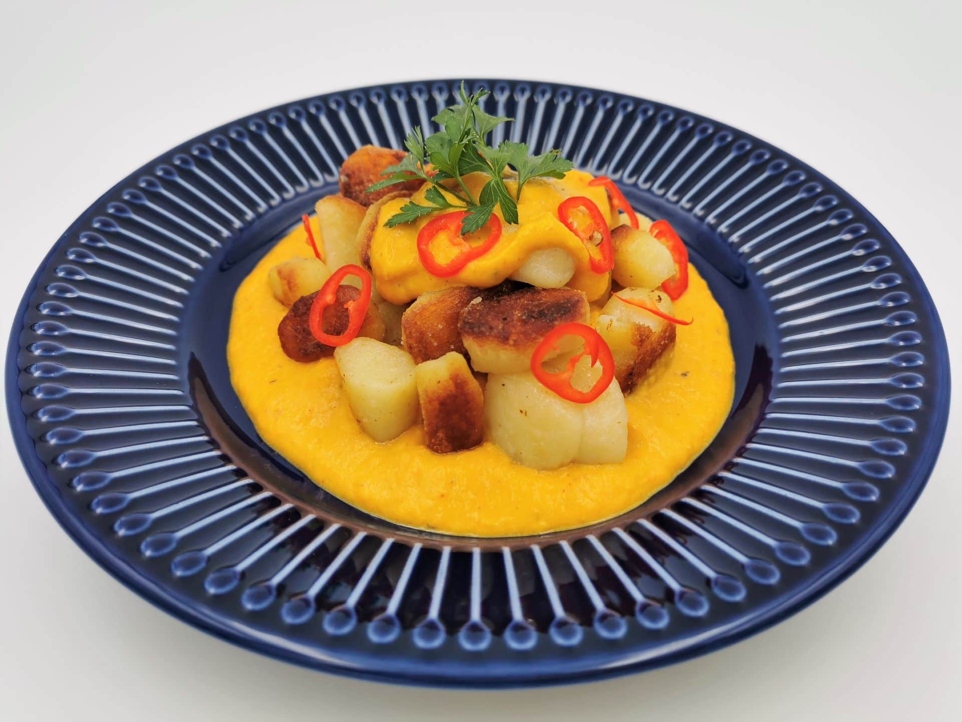 Gnocchi in Paprika-Chili-Sauce, serviert auf einem blauen Teller, garniert mit Chiliringen und Petersilie.