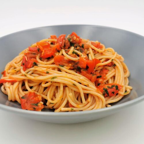 Spaghetti mit geschmorten Tomaten, Chili und Knoblauch angerichtet in einem blauen Teller.