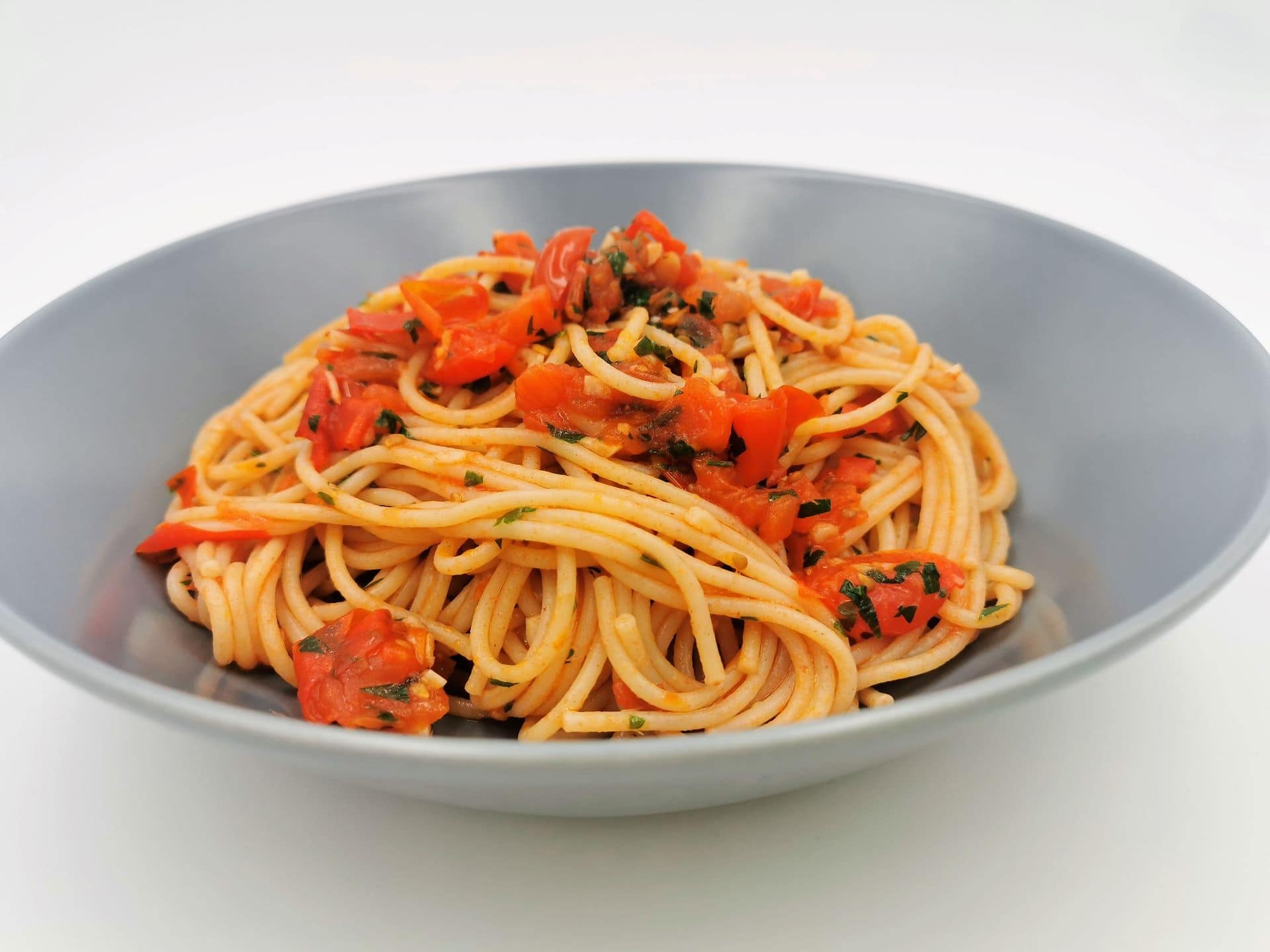 Spaghetti mit geschmorten Tomaten, Chili und Knoblauch angerichtet in einem blauen Teller.
