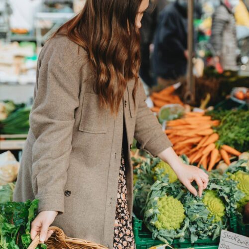 Junge Frau kauft frisches Gemüse am Markt ein