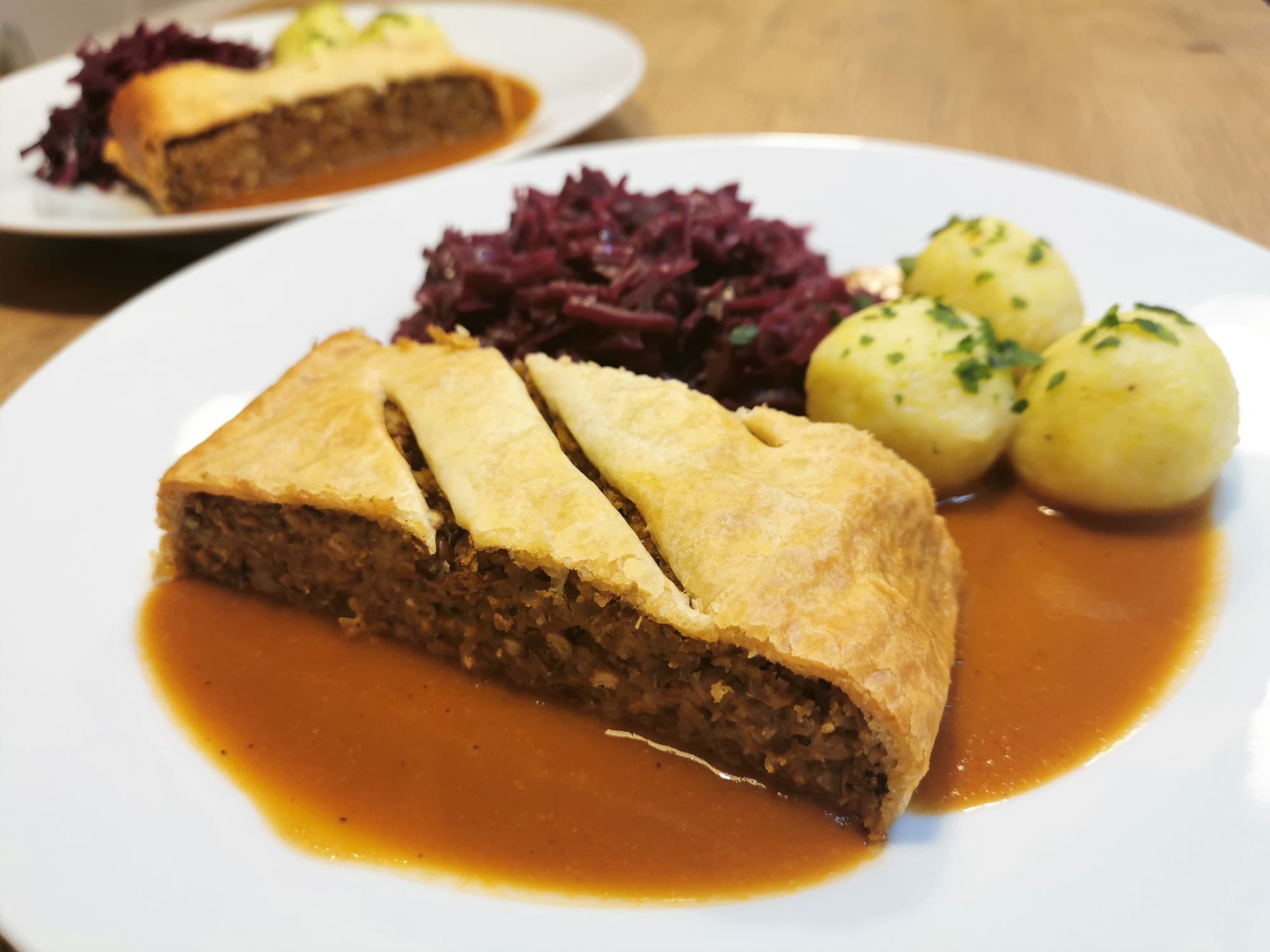 Linsenbraten mit Bratensauce, drei Erdäpfelknödeln und Rotkraut, angerichtet auf einem weißen Teller.