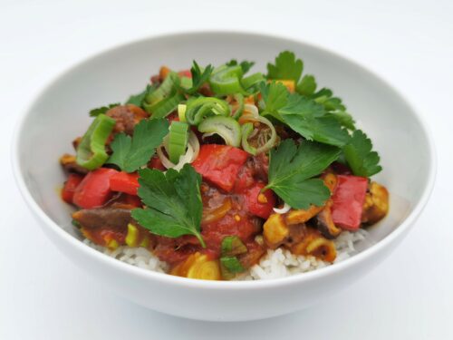 Chili-Gemüse mit Tofu-Paneer angerichtet in einer weißen Schale, garniert mit Frühlingszwiebelringen und Petersilienblättern.